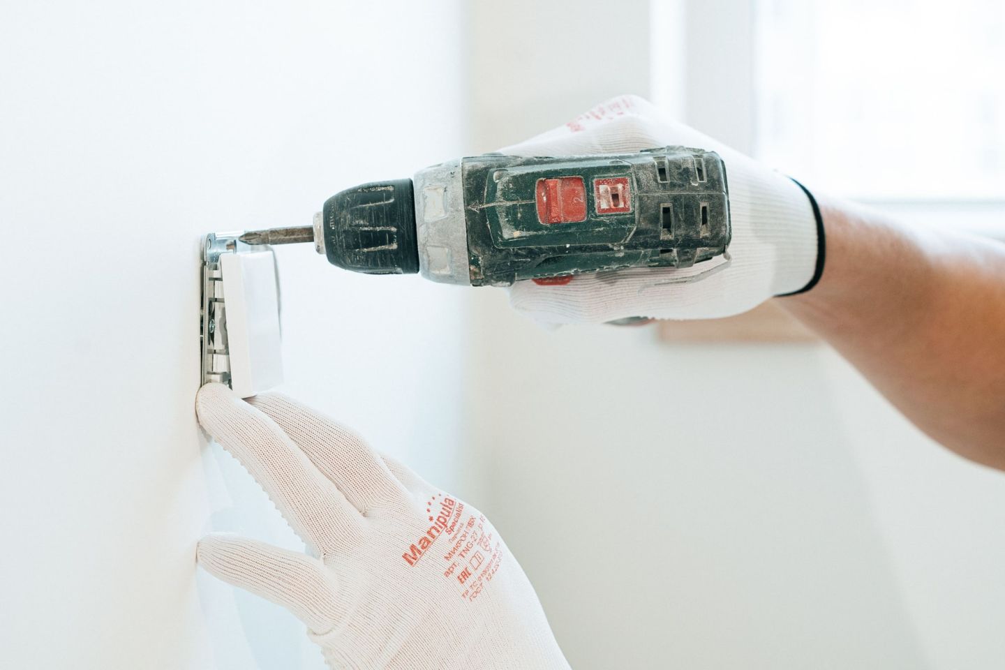 Monteur mit Arbeitshandschuhen befestigt eine Halterung mit dem Akkuschrauber an einer Wand.